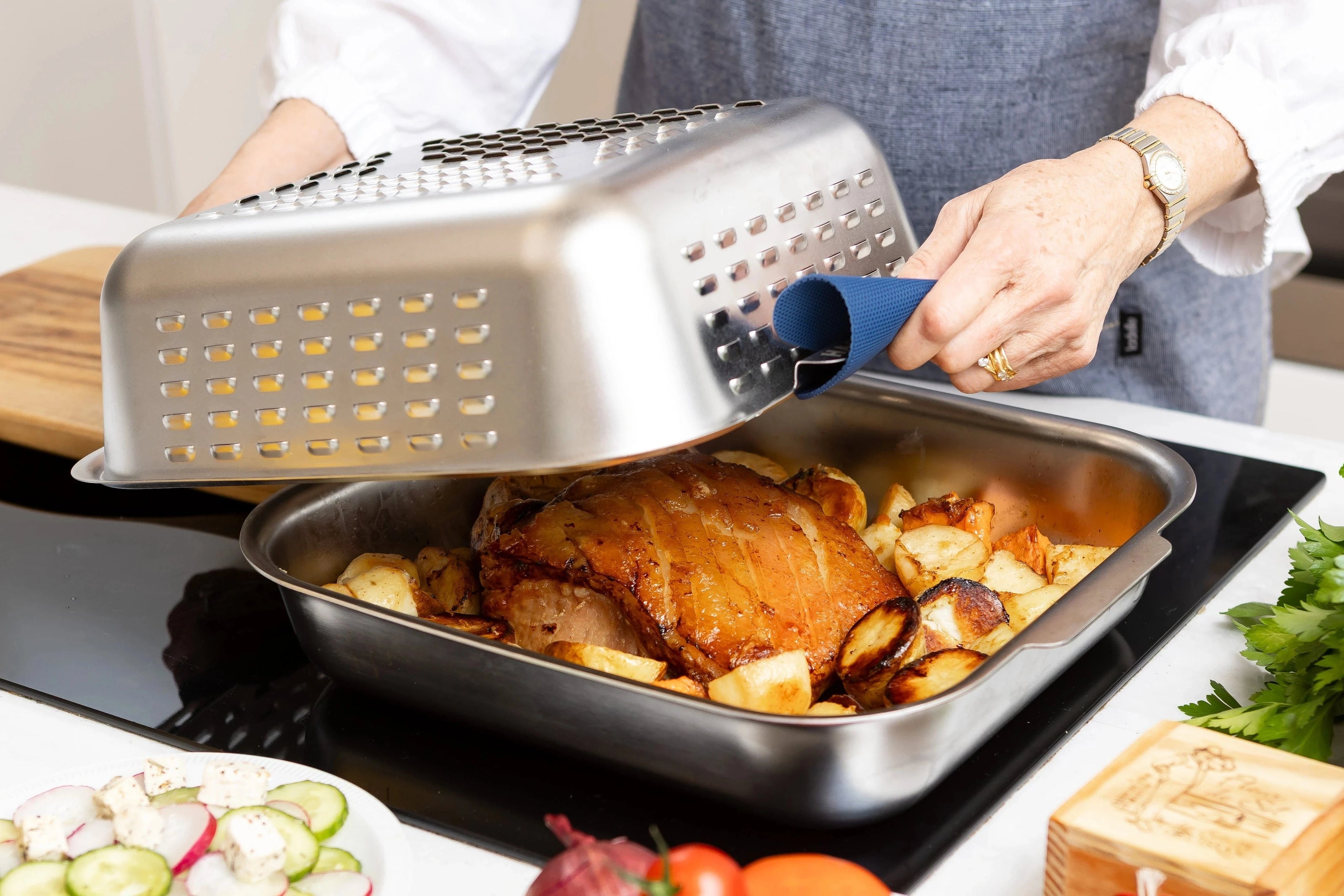 Stainless steel spatter guard cover being lifted off perfectly cooked pork roast. Roast more. Clean Less. With the Hagane Home Ultimate Roaster.